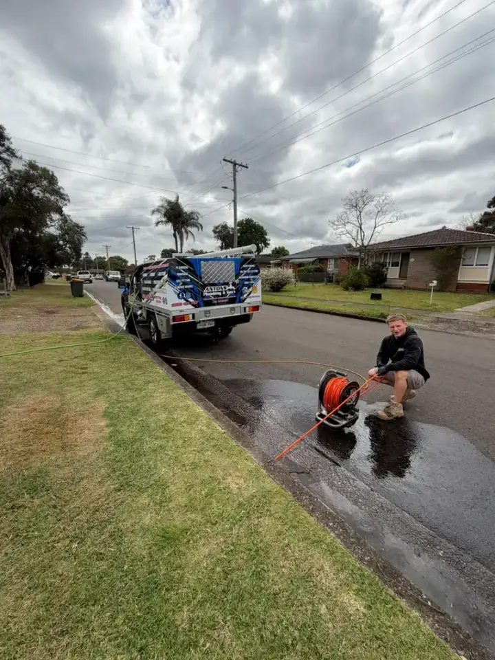 Plumber working with drain-clearing equipment beside a service vehicle