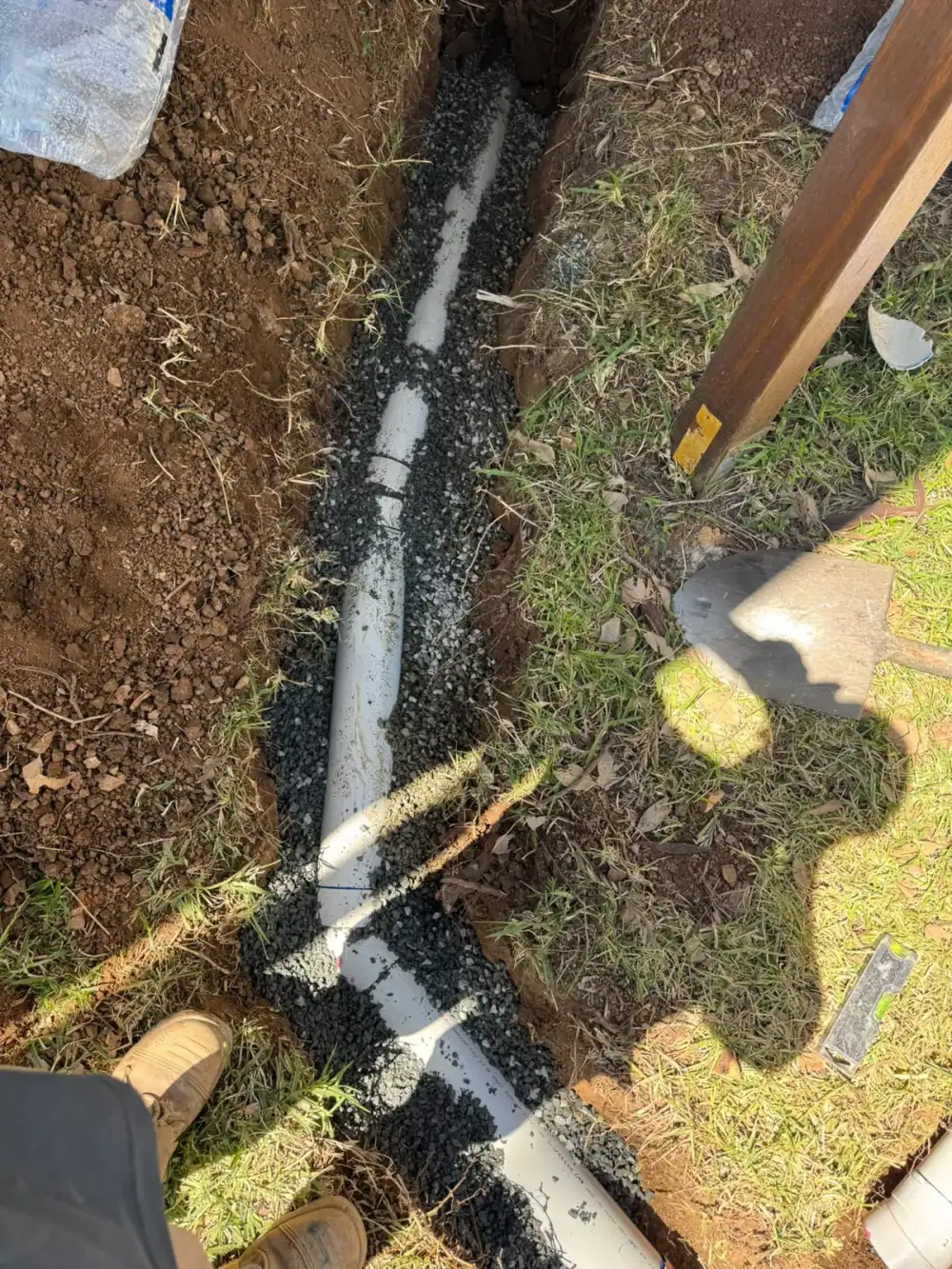White drainage pipe laid on gravel bedding in an open garden trench