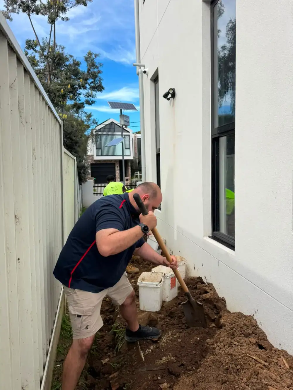 Antons plumber excavating a narrow passage between a house and fence