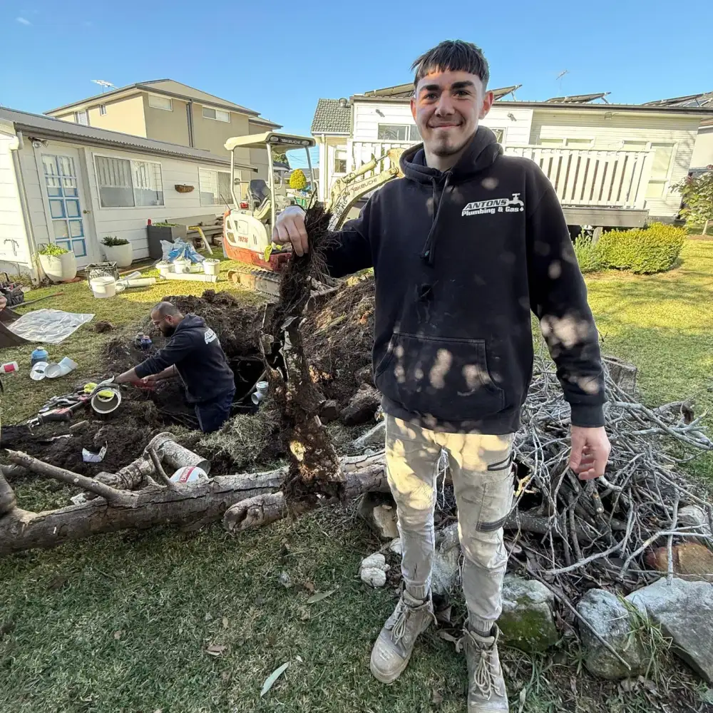 Antons technician showing removed roots with the drainage excavation behind him