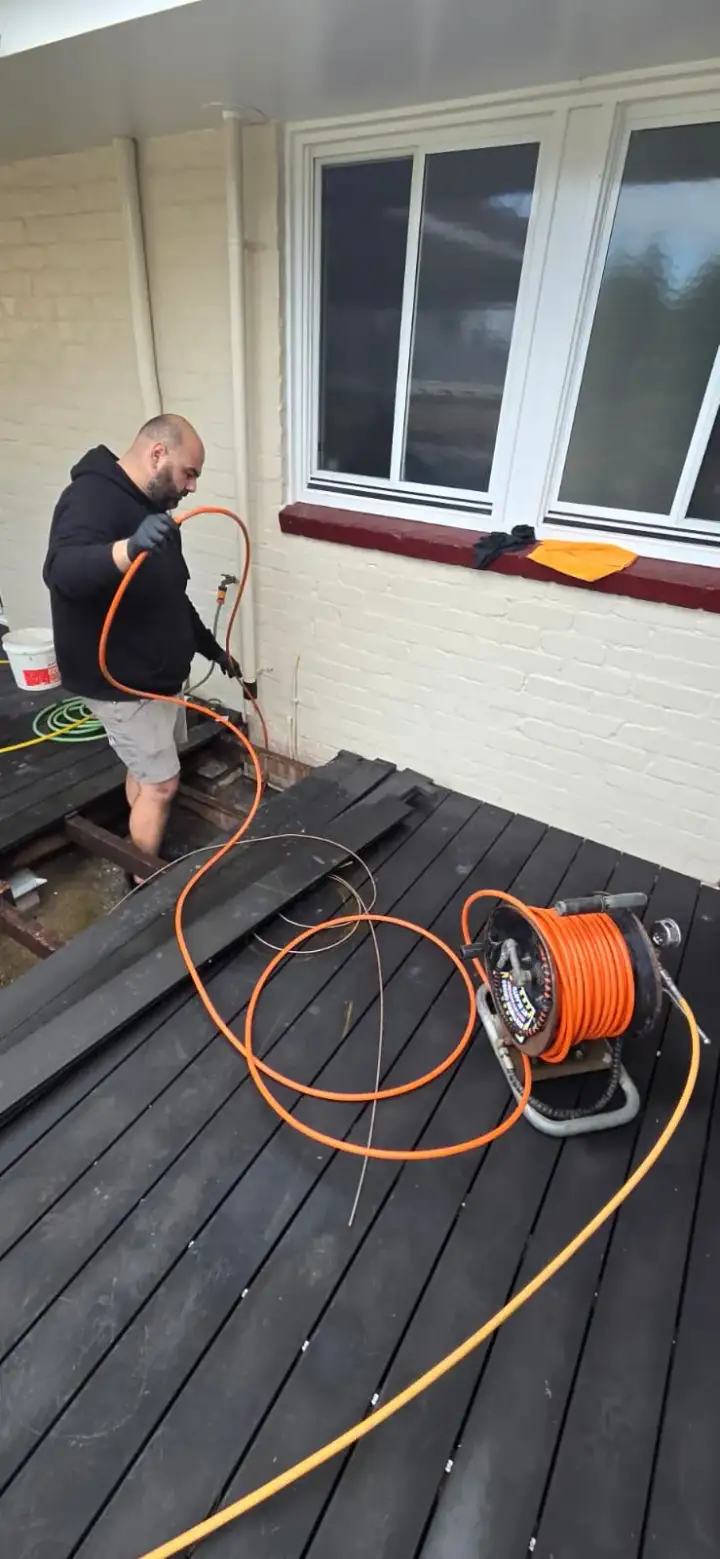Plumber using drain equipment through an opening in a timber deck