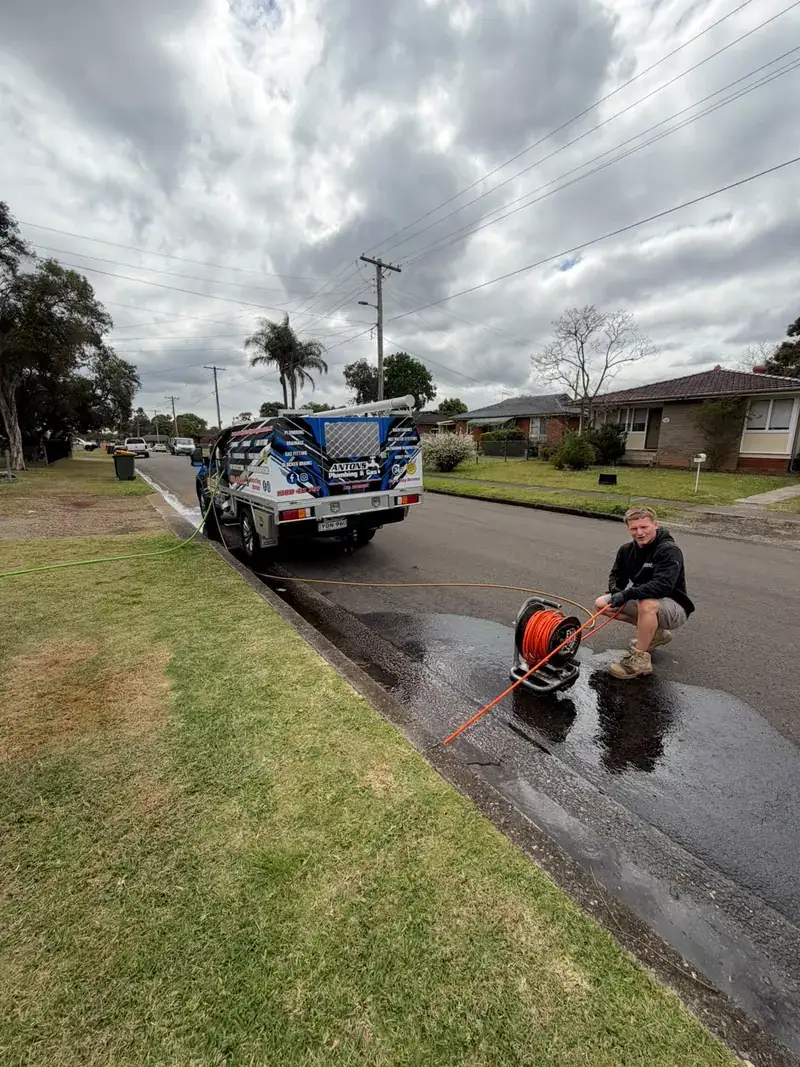 Plumber working with drain-clearing equipment beside a service vehicle