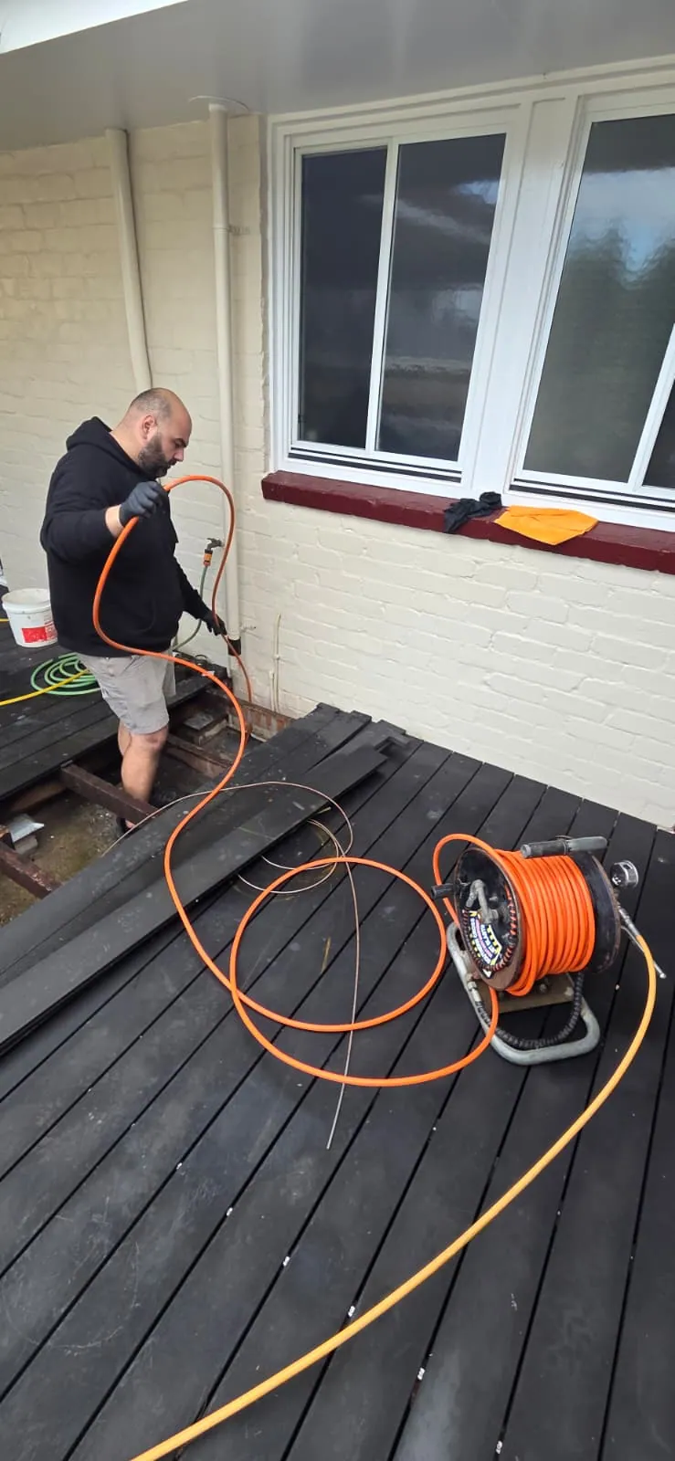 Plumber using drain equipment through an opening in a timber deck